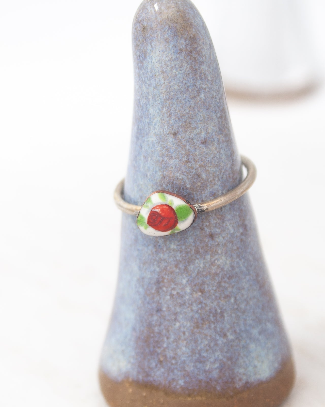 A ring with a red and green stone is displayed on a blue ceramic stand.