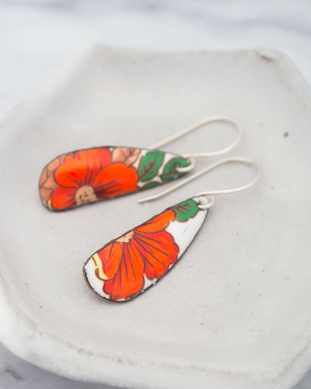 A pair of earrings with a floral design, featuring red and orange flowers on a white background.