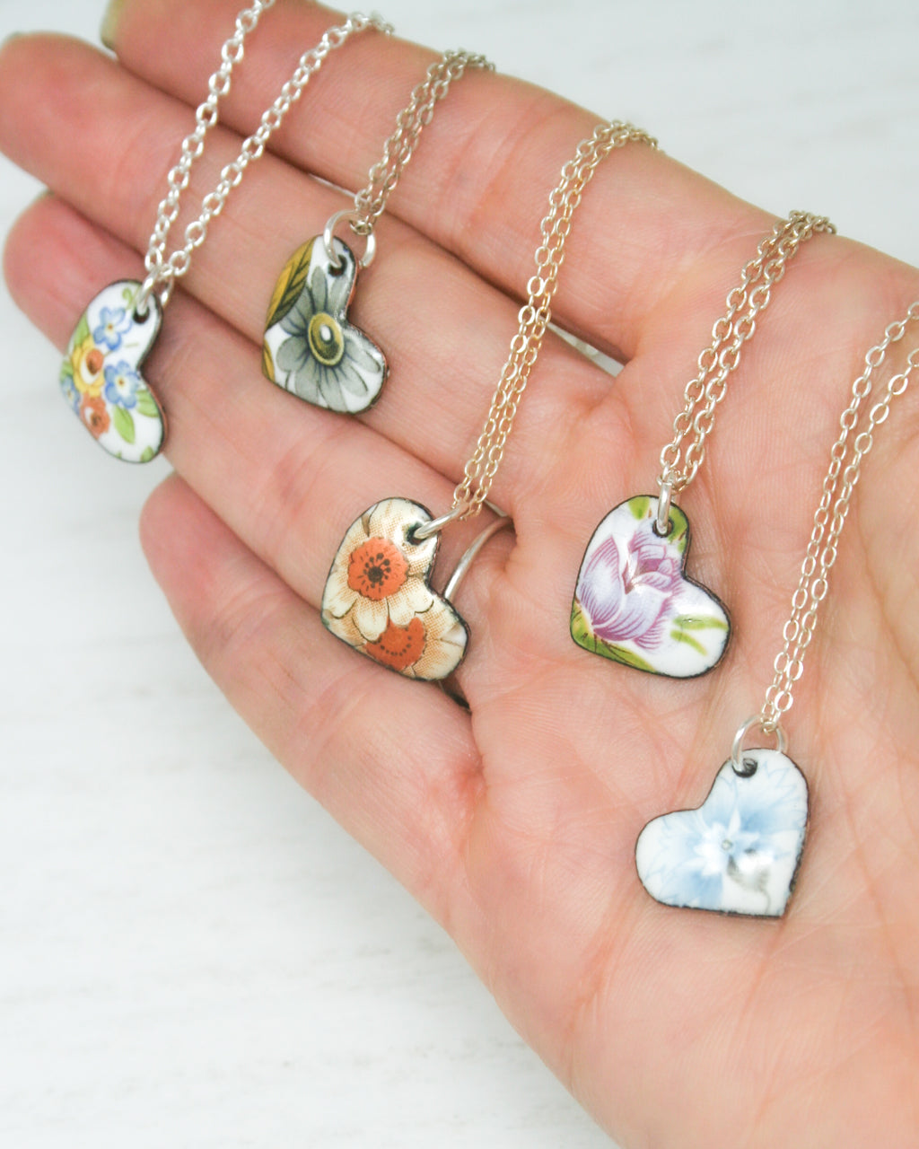 a person's hand holding five different necklaces