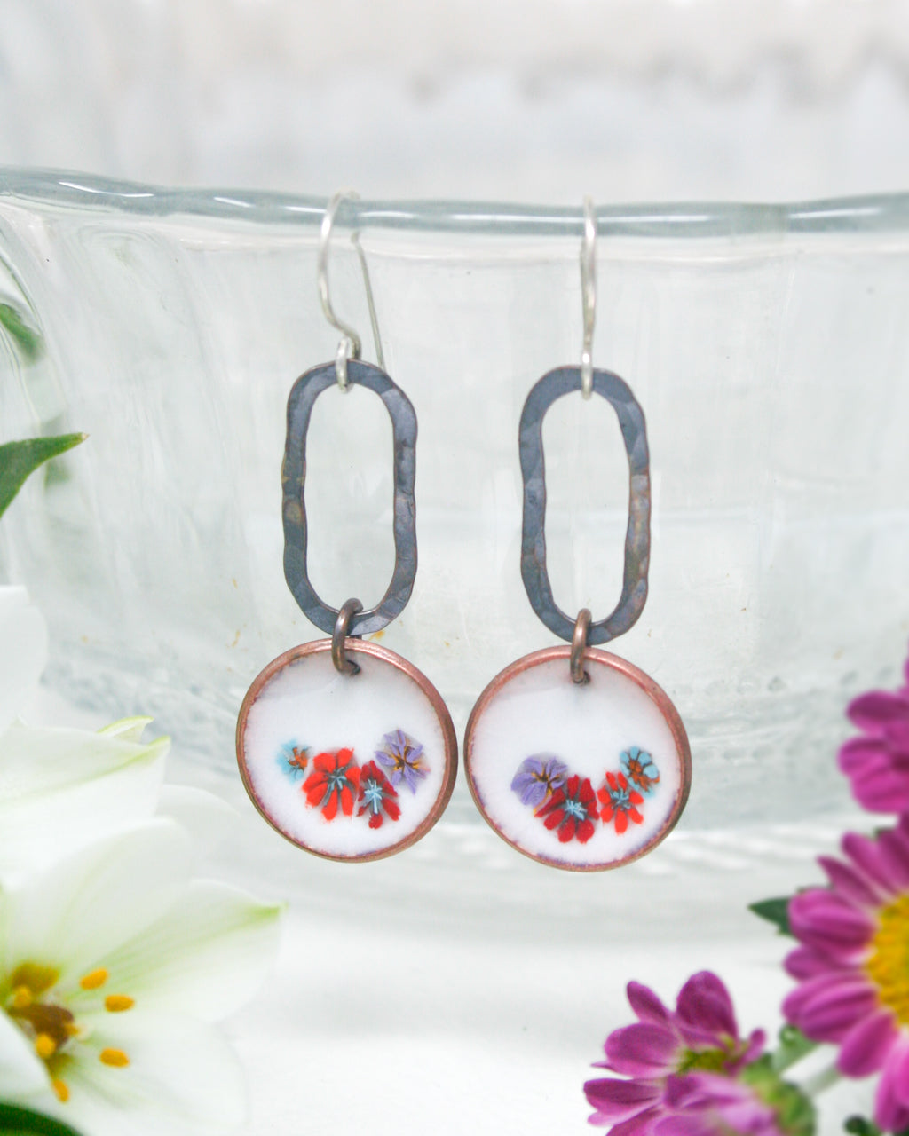 a pair of earrings with flowers in the background