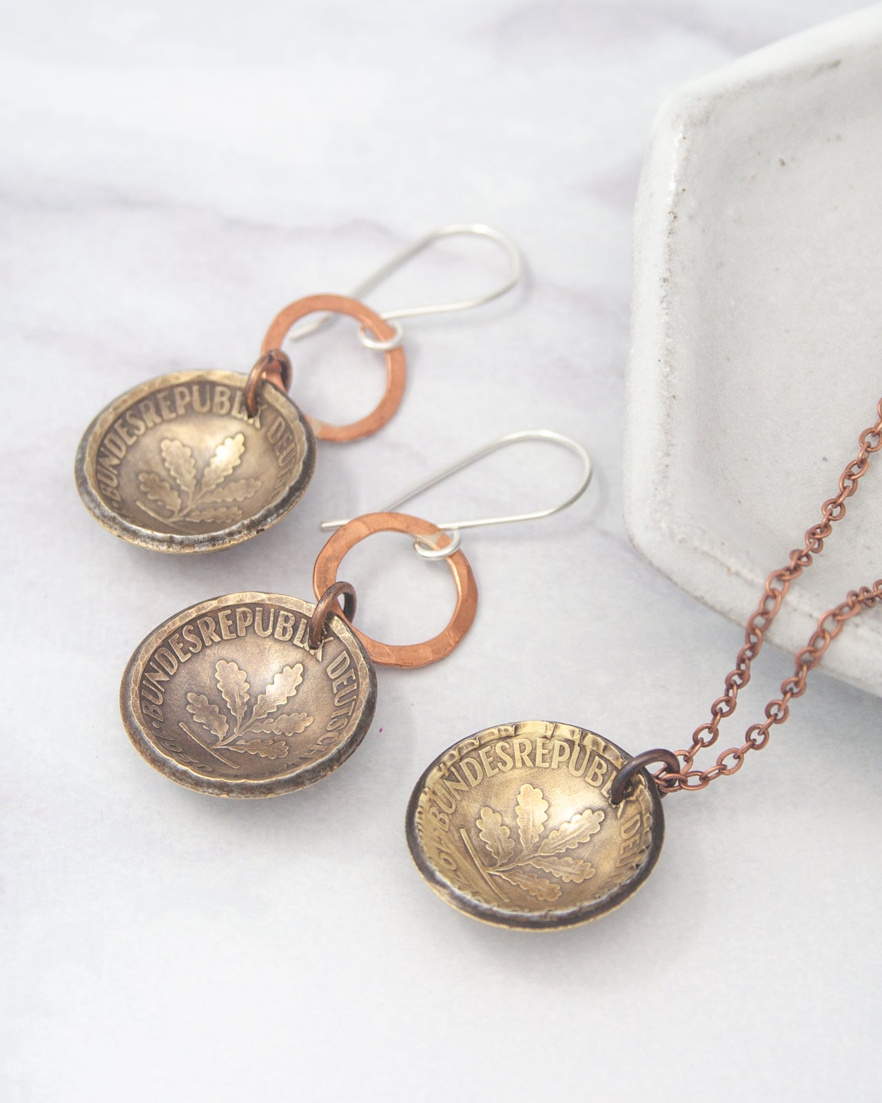 a pair of earrings and a necklace with a pendant, all made of metal and displaying a leaf design.