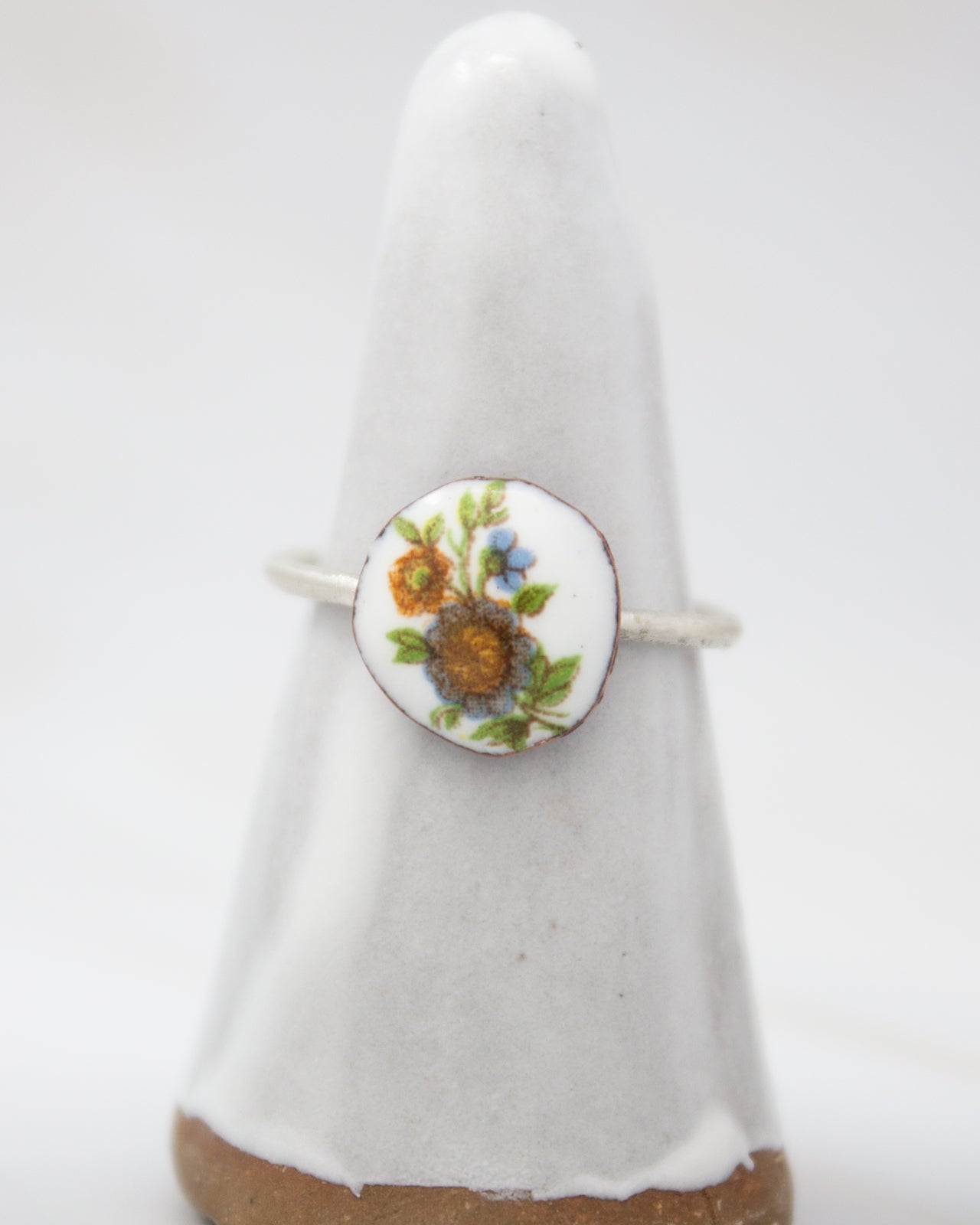 A white ceramic ring with a floral design on it, placed on a white pedestal.
