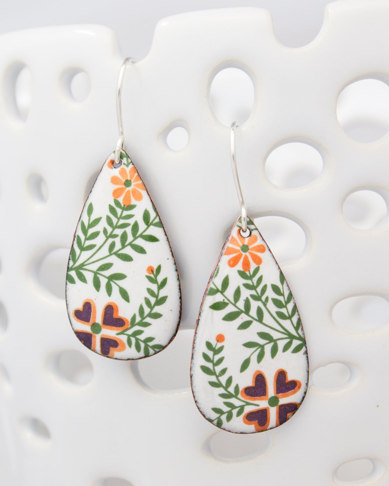 A pair of earrings with a floral design, featuring orange and green leaves and purple flowers.