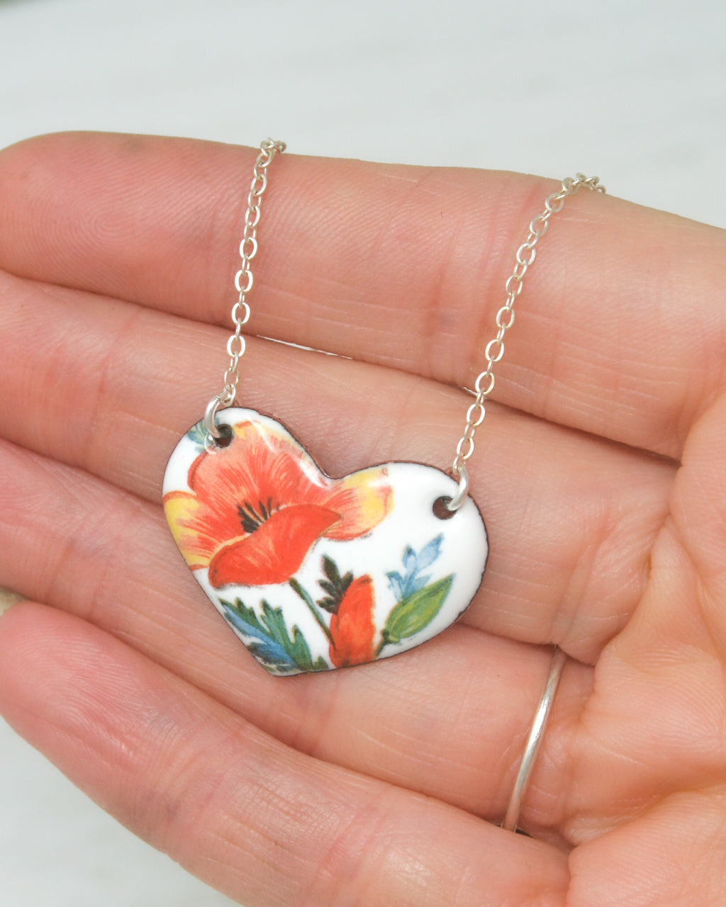 a hand holding a heart shaped necklace with flowers on it