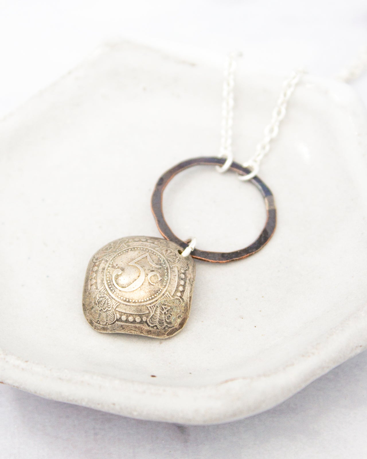 A silver necklace with a pendant featuring an ornate design, resting on a white surface.