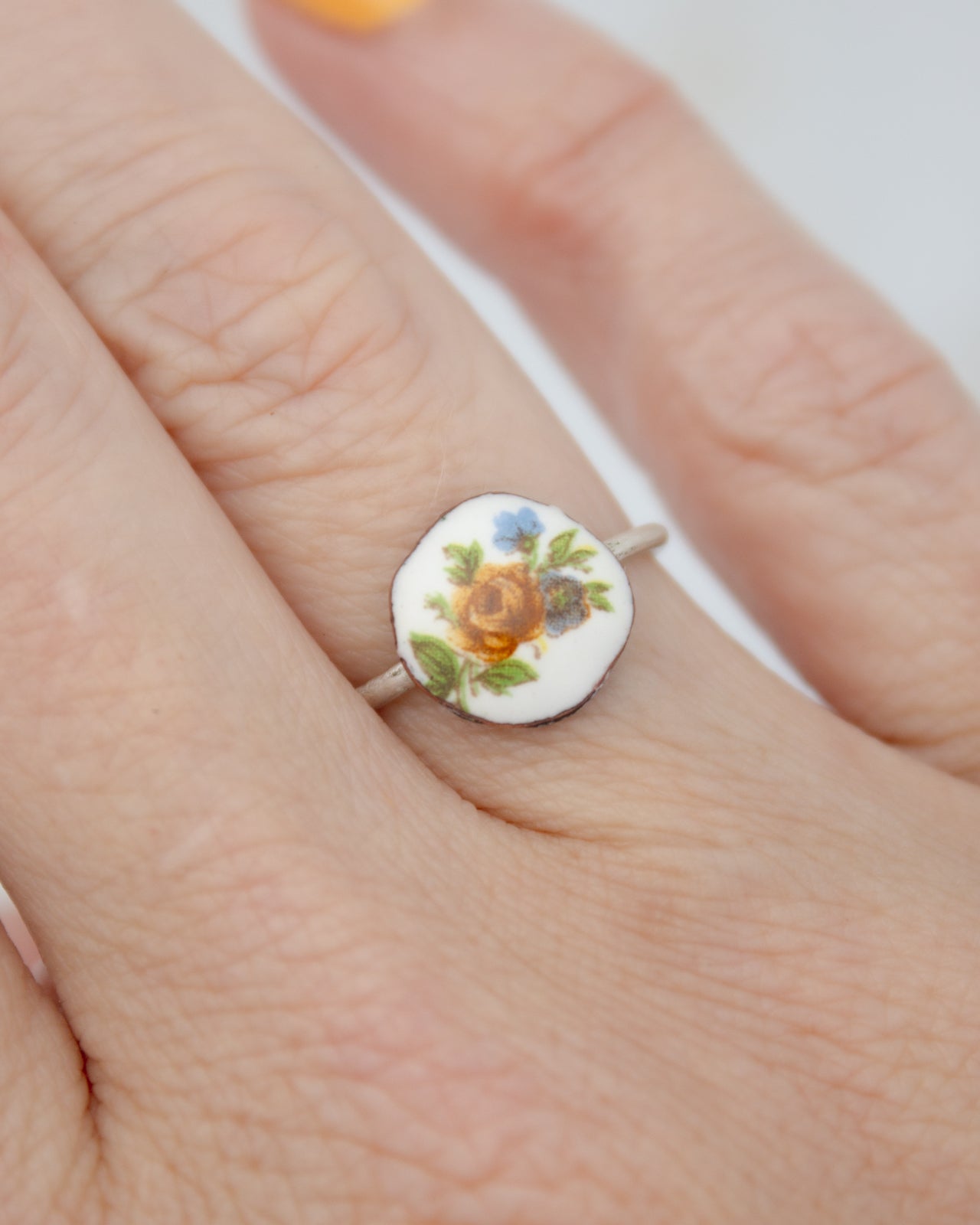 A close-up of a person's hand wearing a ring with a floral design on the finger.