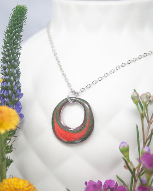 A necklace with a colorful pendant is displayed in a white vase, surrounded by various flowers.