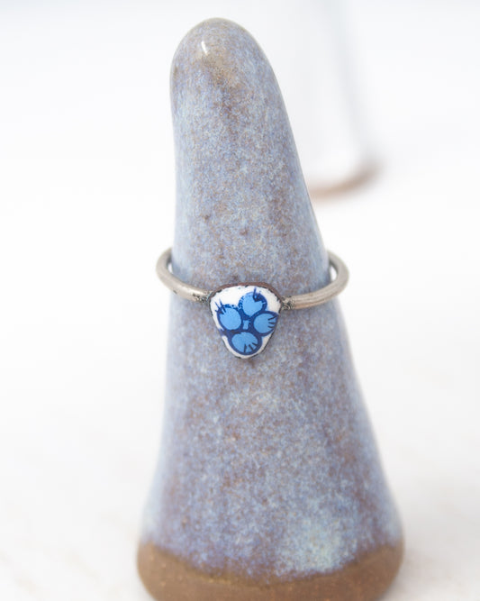 A ring with a blue floral design on it, displayed on a gray ceramic stand.