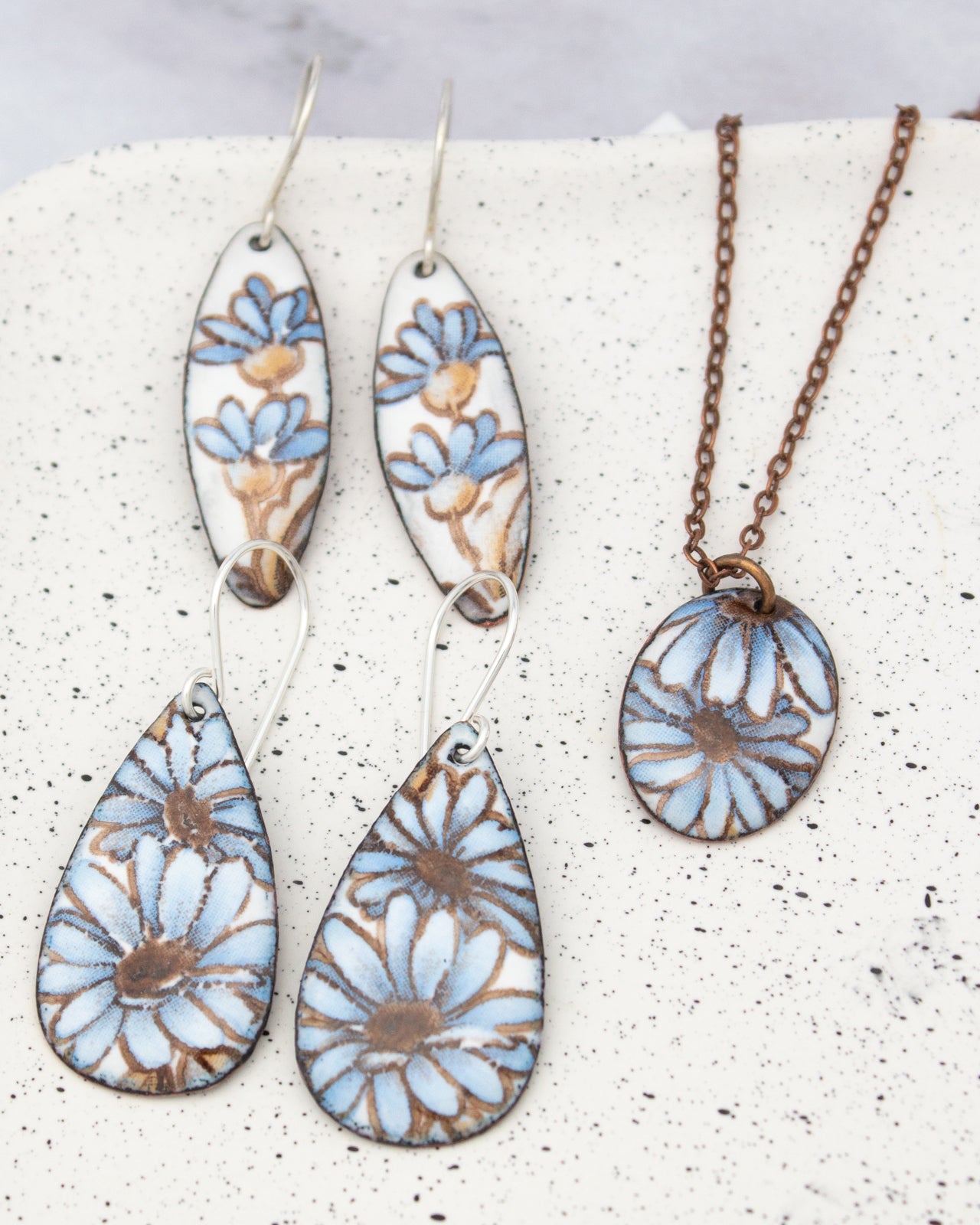 a pair of earrings and a necklace featuring blue and brown floral designs.