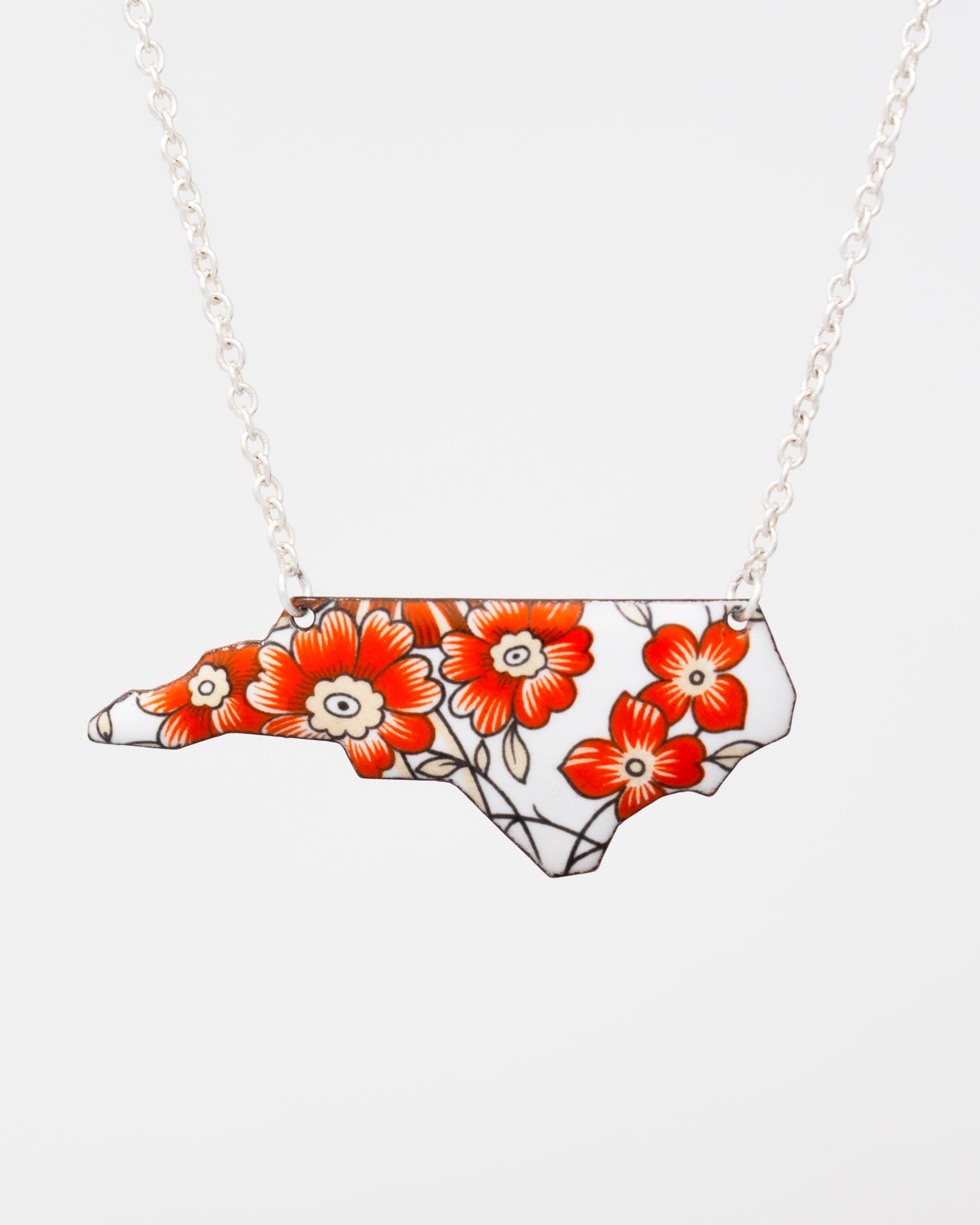 A necklace with a pendant in the shape of the state of North Carolina, featuring a floral design in red and orange colors.