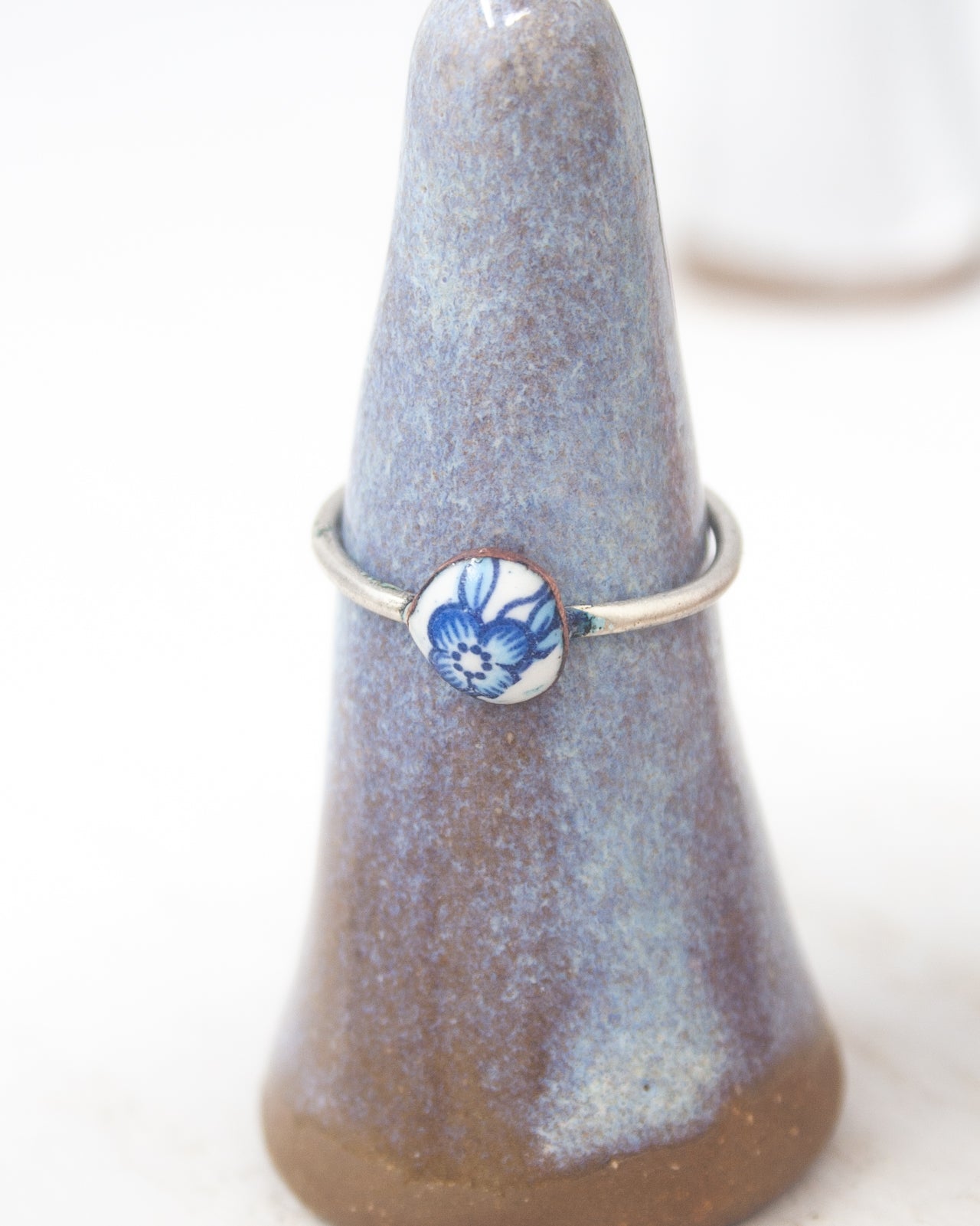 A ring with a blue floral design on it, displayed on a ceramic stand.