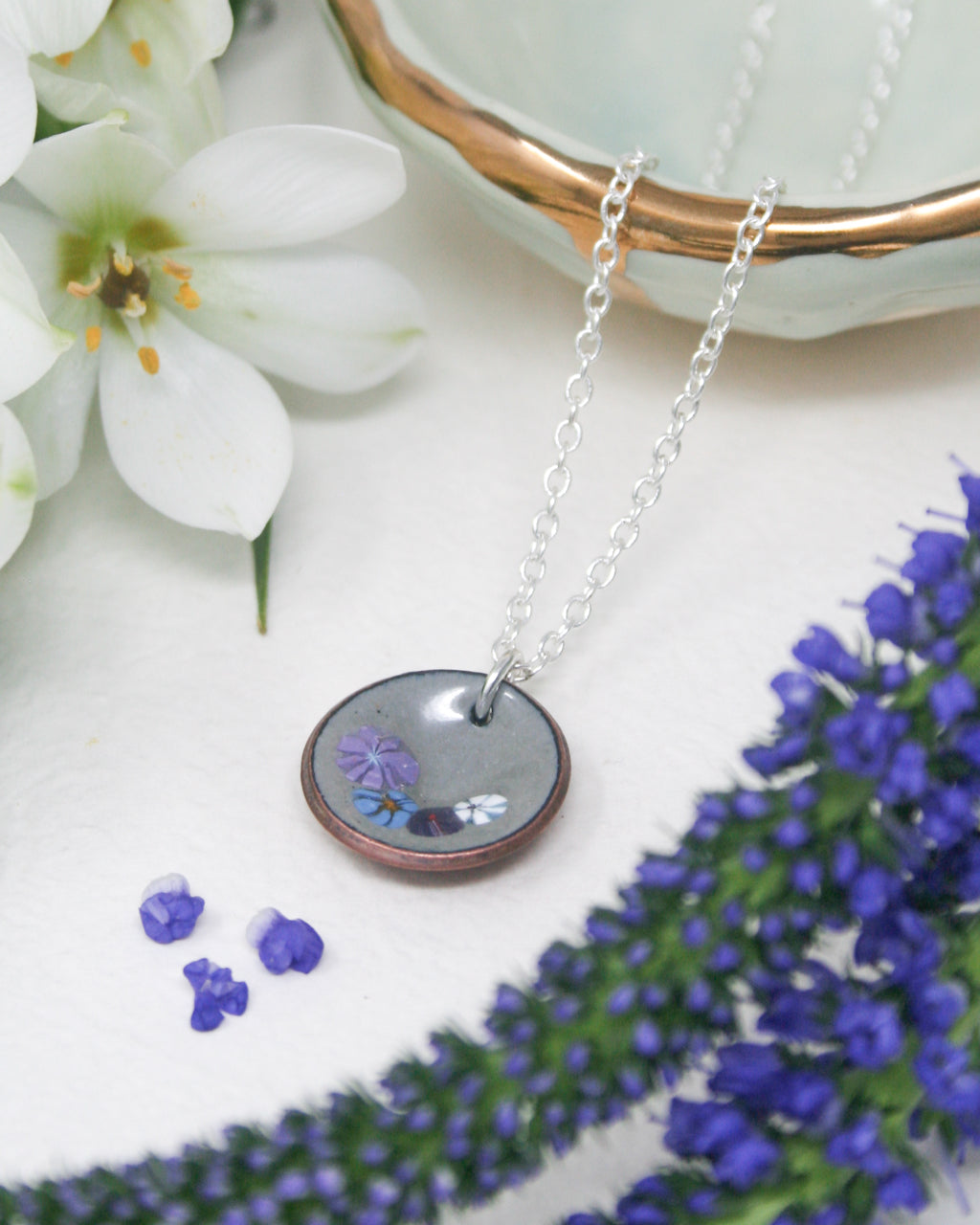 a close up of a necklace on a table with flowers