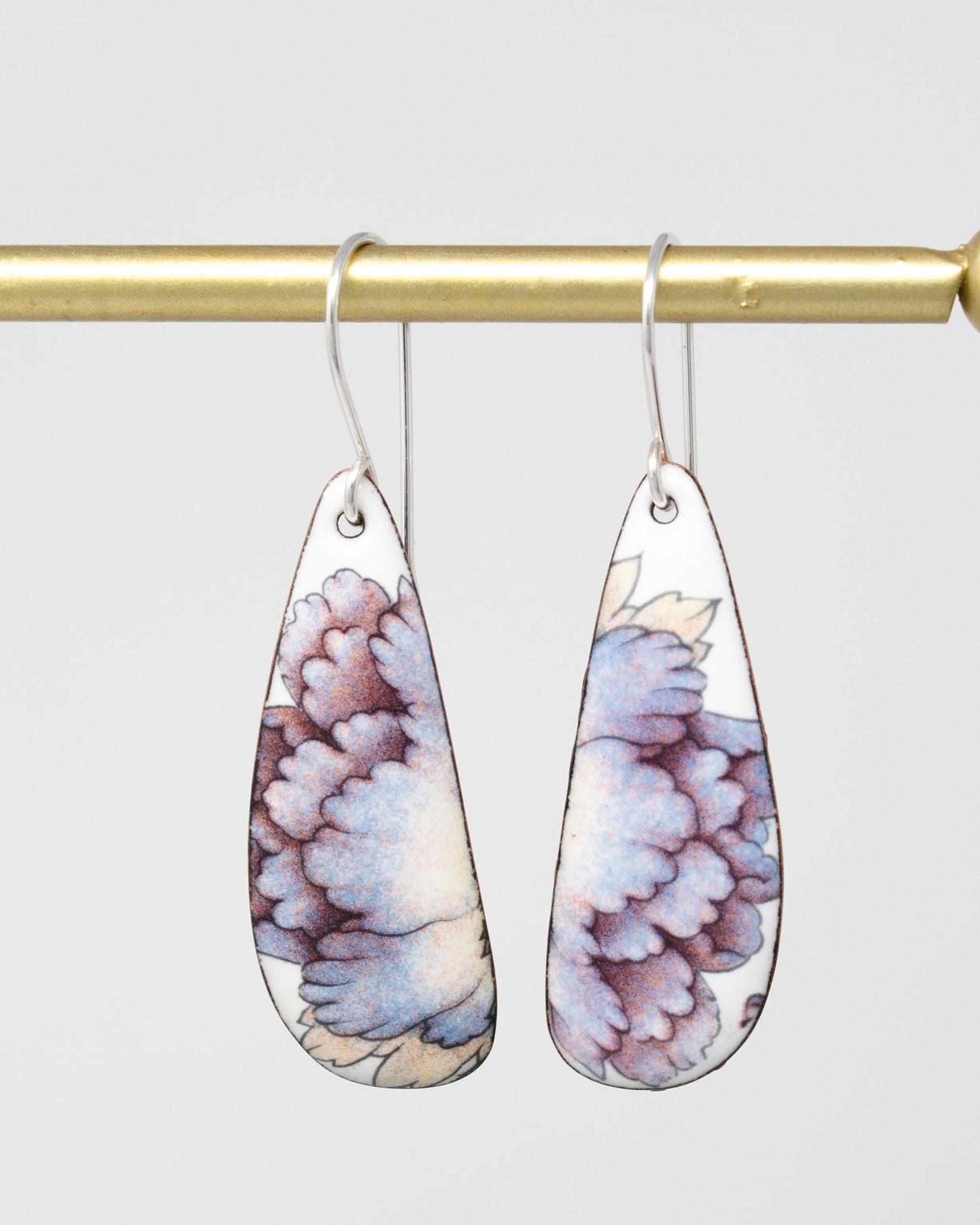 A pair of earrings with a floral design hanging from a gold-colored metal hook.