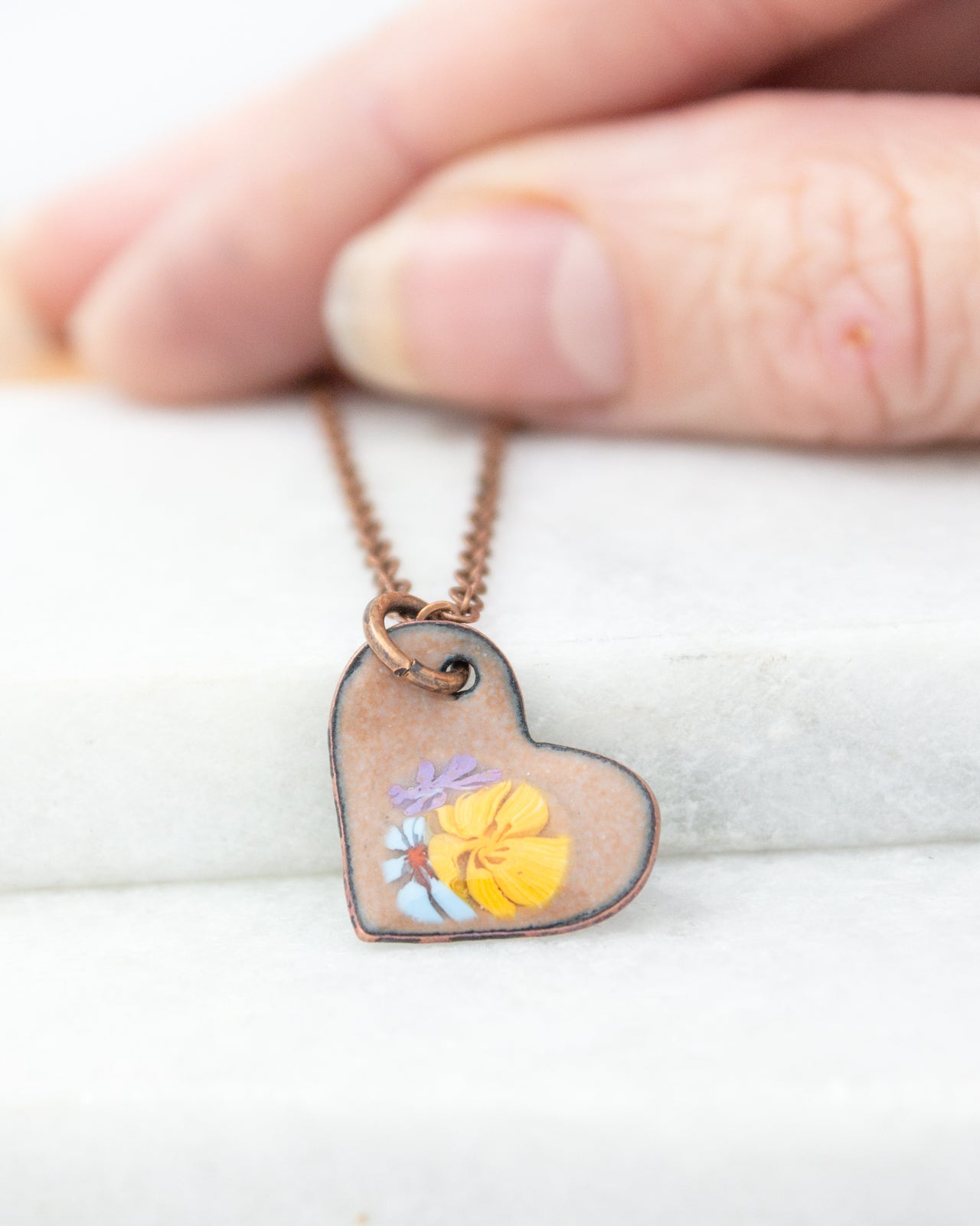 A hand is holding a heart-shaped pendant necklace with a floral design.