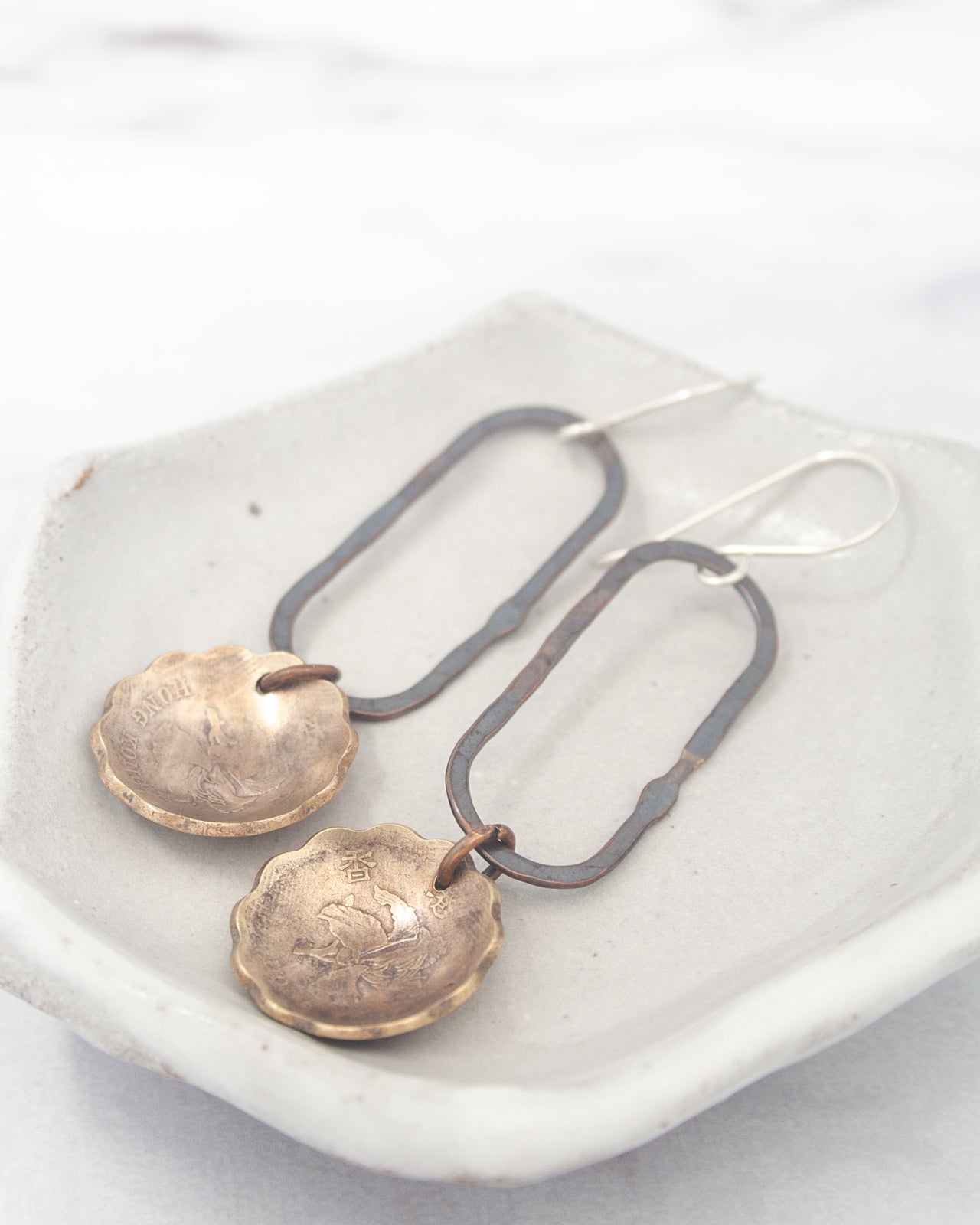 A pair of earrings with a metal frame and a metal pendant, resting on a white surface.