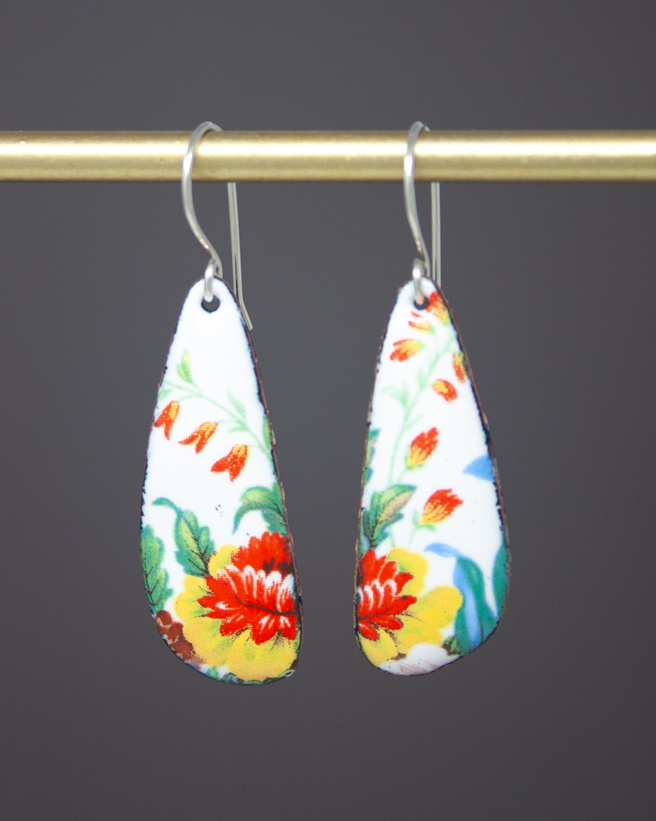A pair of earrings with a floral design hanging from a gold-colored metal hook.