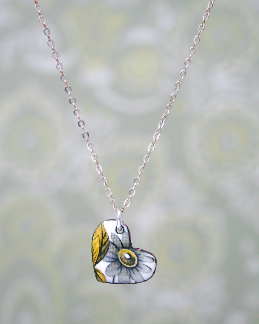 A silver necklace with a heart-shaped pendant featuring a white flower design.
