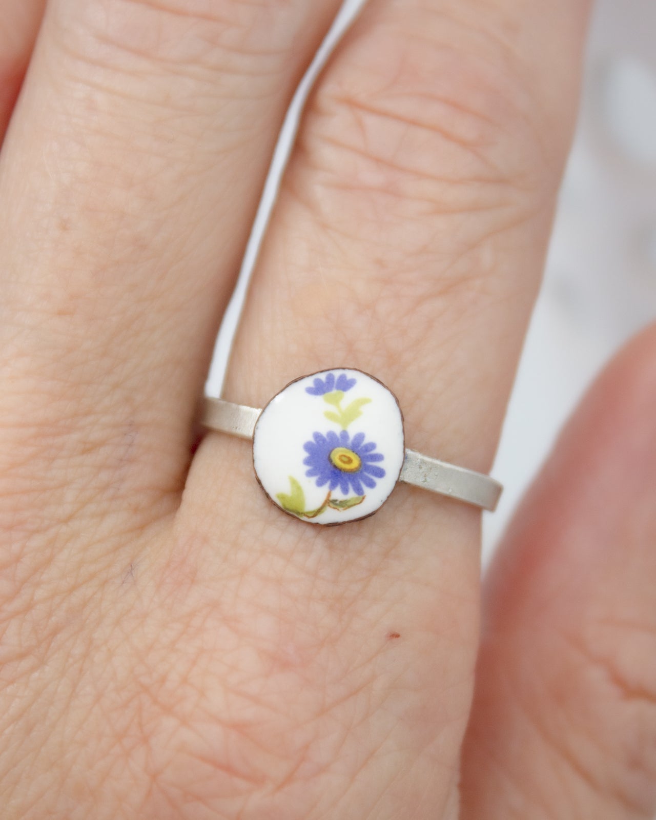 A close-up of a person's hand wearing a ring with a small, round, floral-patterned metal piece.