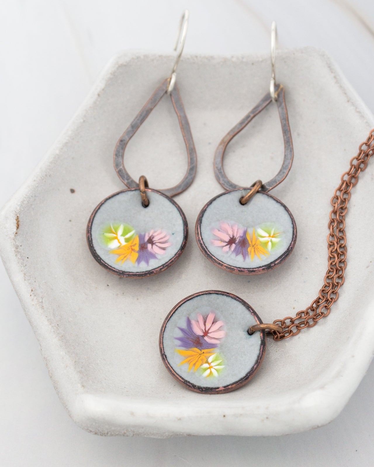 A pair of earrings and a necklace are displayed on a white plate, with the earrings featuring a floral design and the necklace having a chain.