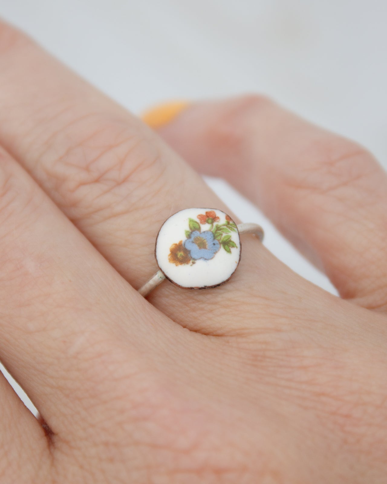 A close-up of a person's hand wearing a ring with a floral design on it.