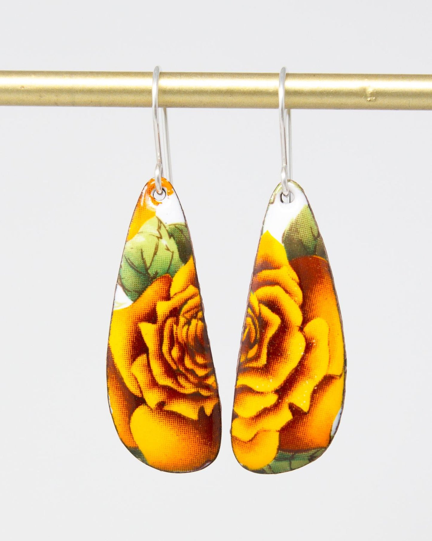 A pair of earrings with a floral design, featuring yellow and orange flowers on a gold-colored metal bar.