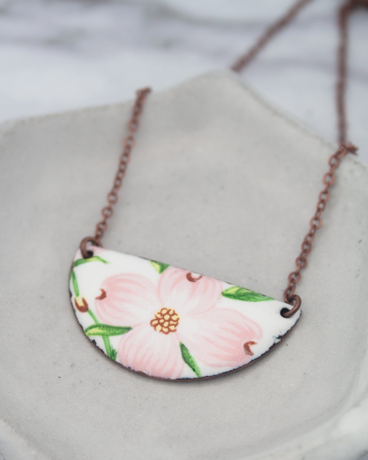 A necklace with a pendant featuring a pink flower design.