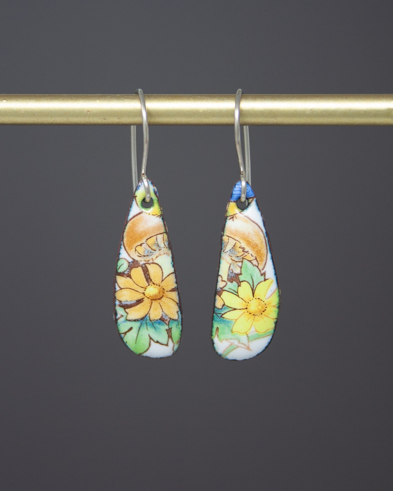 A pair of earrings with colorful floral designs hanging from a gold-colored metal hook.