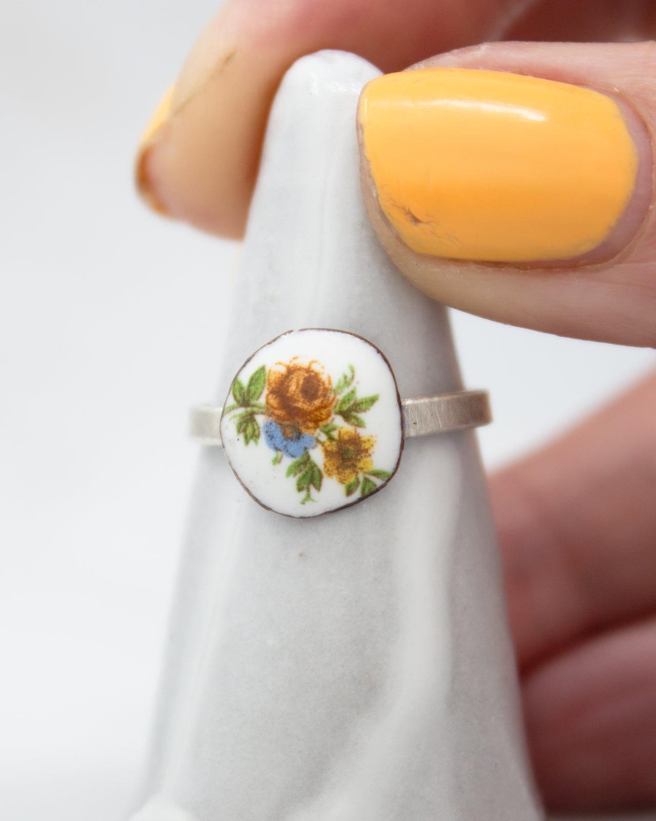 A hand holding a white ring with a floral design on it.