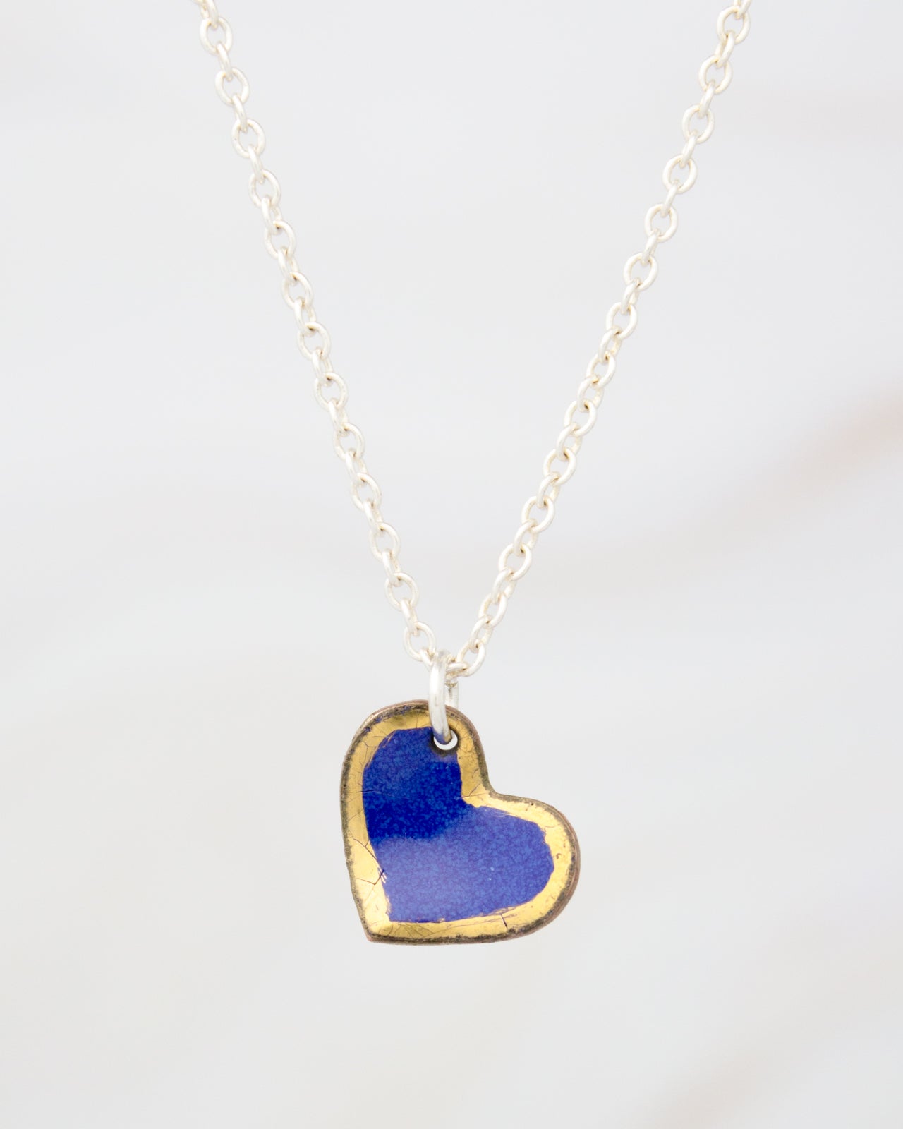A delicate silver necklace with a heart-shaped pendant in a striking blue and gold color scheme.