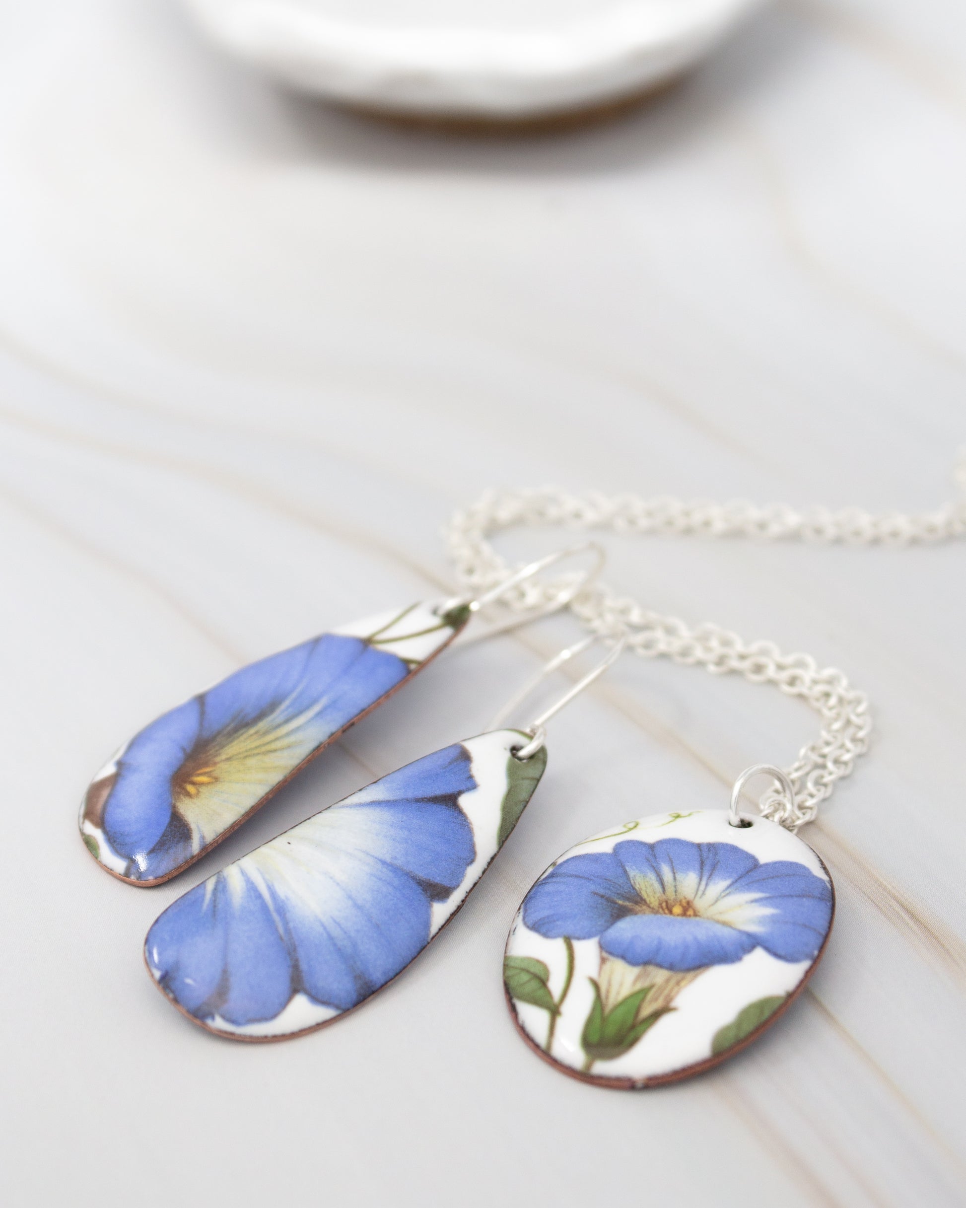 a pair of earrings and a necklace with blue and white floral designs.