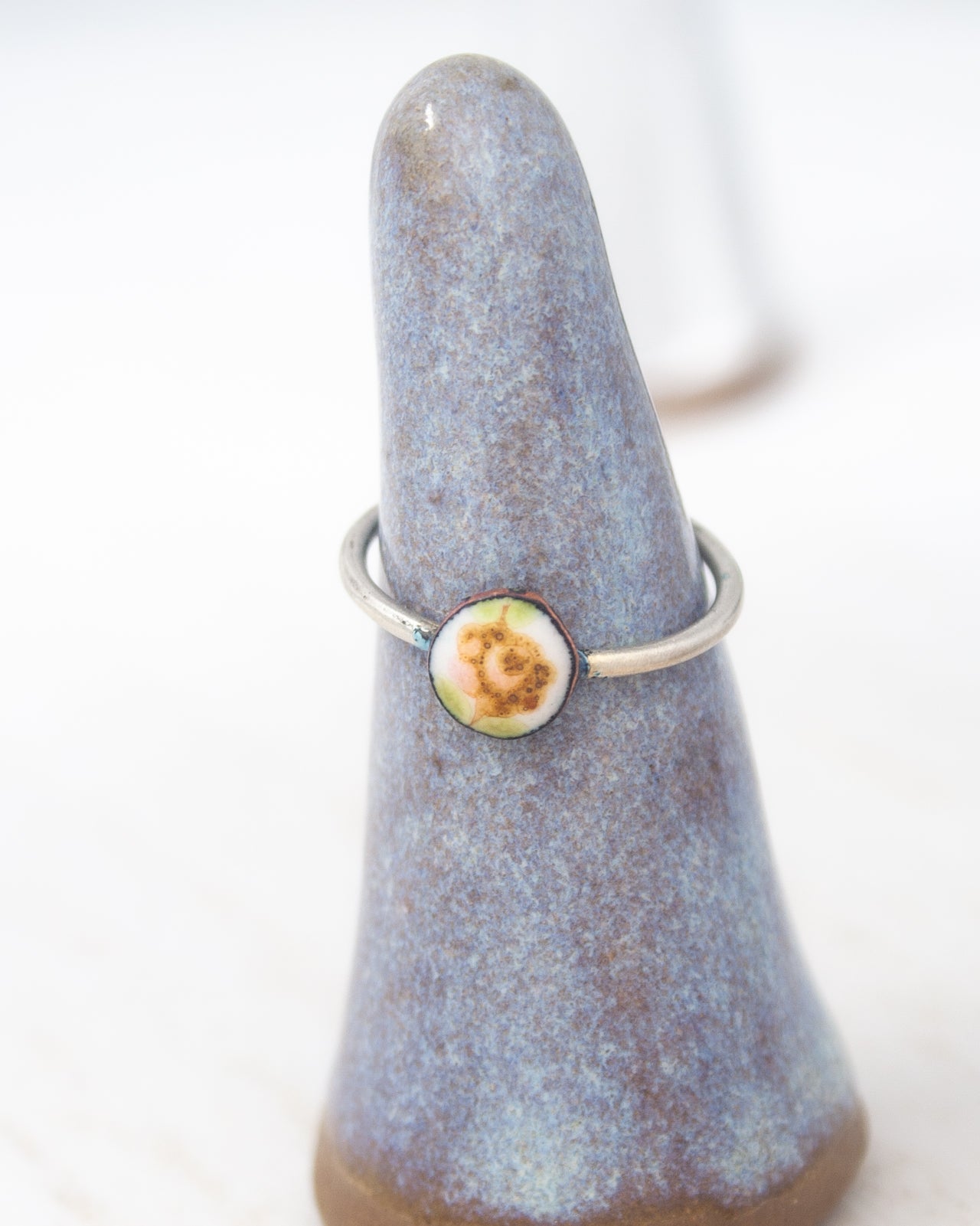 A ring with a flower design on it, displayed on a blue ceramic ring holder.