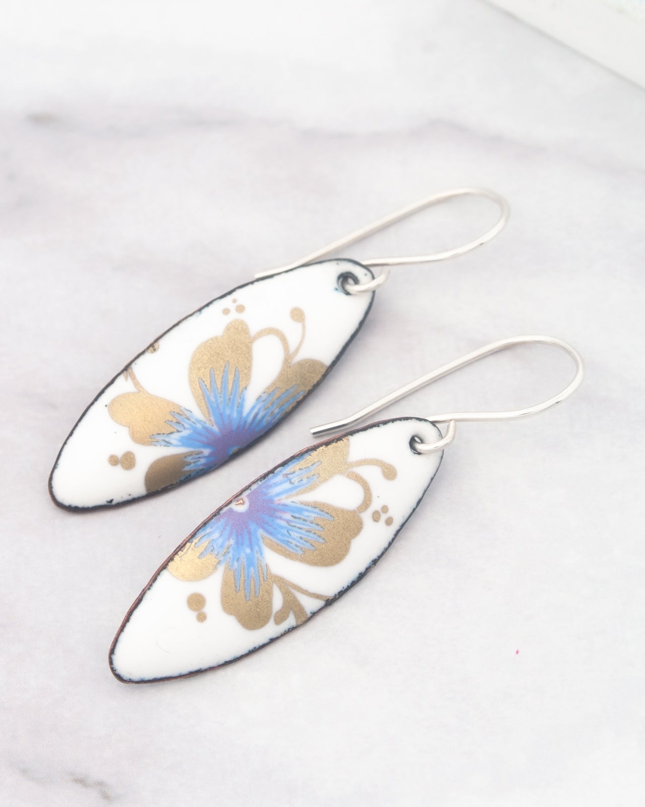 A pair of white earrings with blue and gold floral designs.