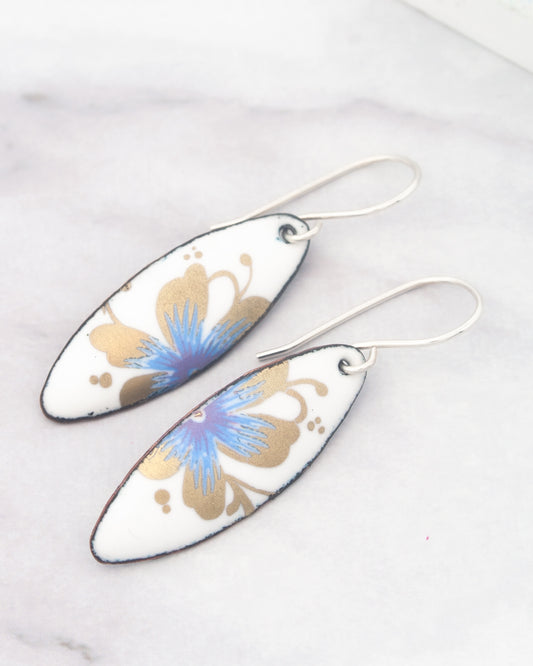 A pair of white earrings with blue and gold floral designs.