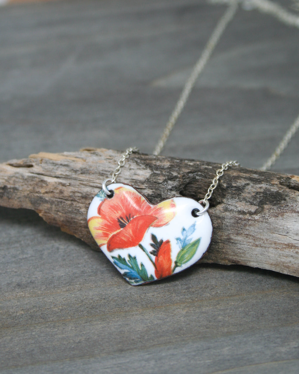 A heart-shaped pendant necklace with a floral design, resting on a wooden surface.