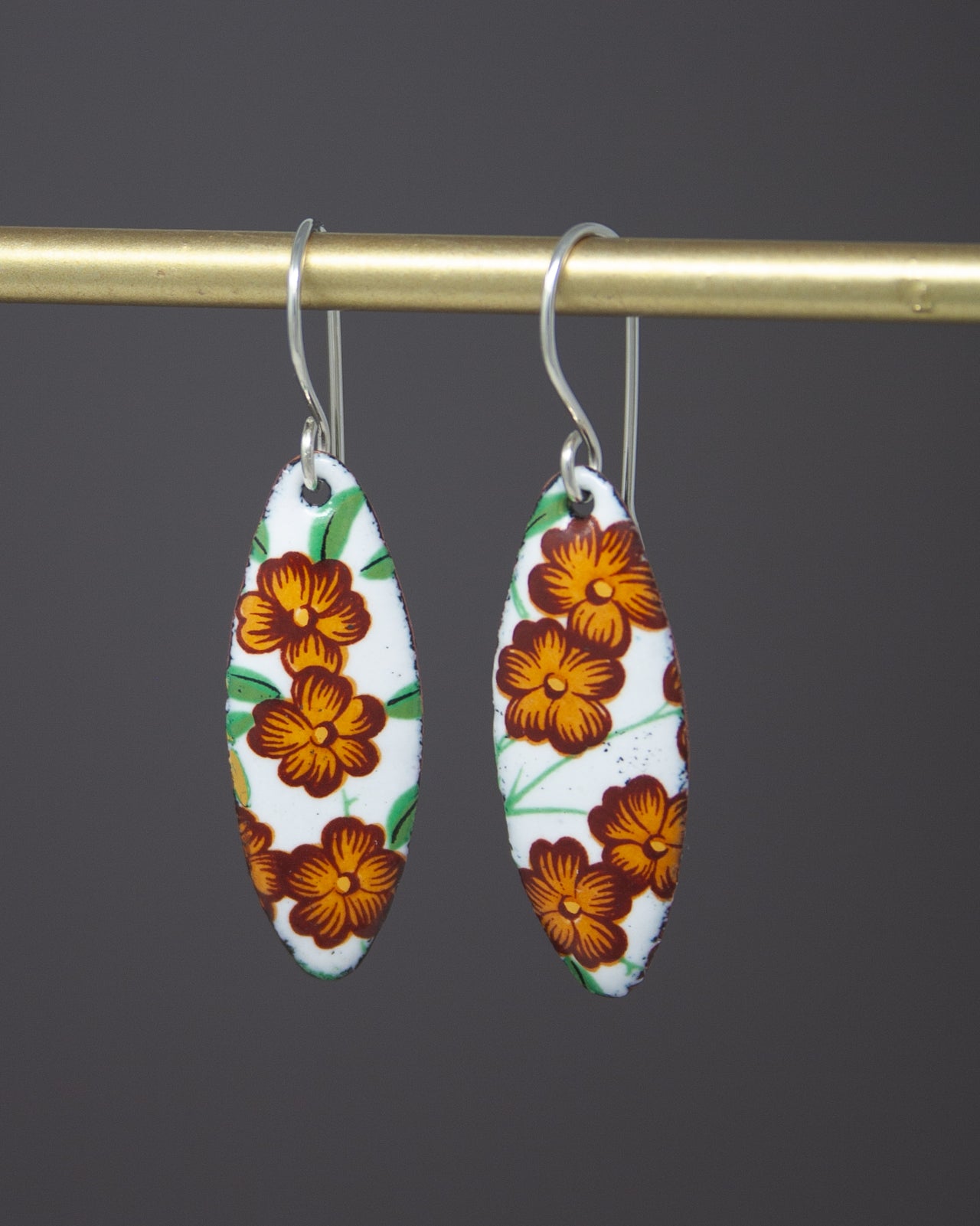 A pair of earrings with a floral design, featuring orange and white flowers on a white background.