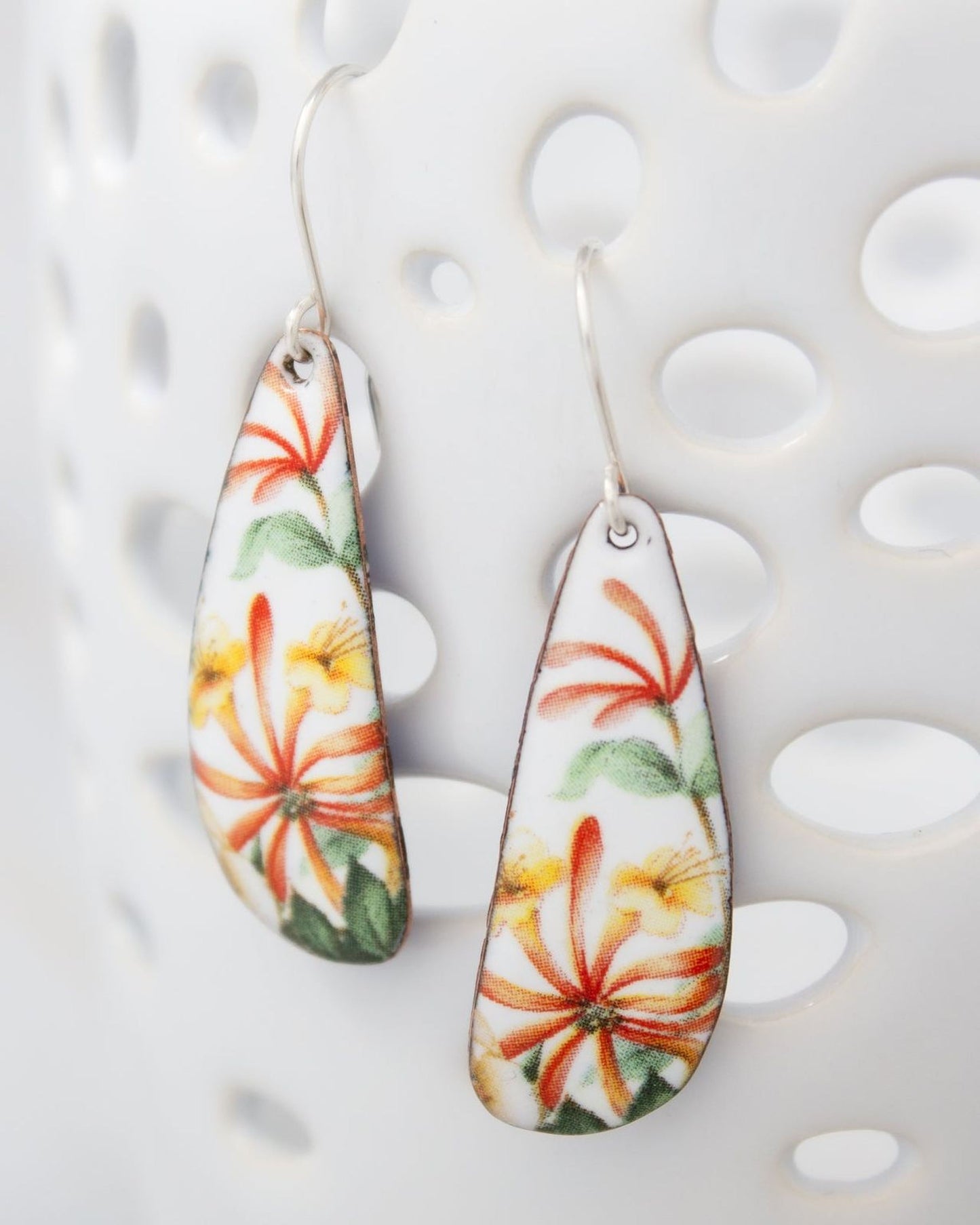 A pair of earrings with a floral design, featuring vibrant orange and yellow flowers against a white background.