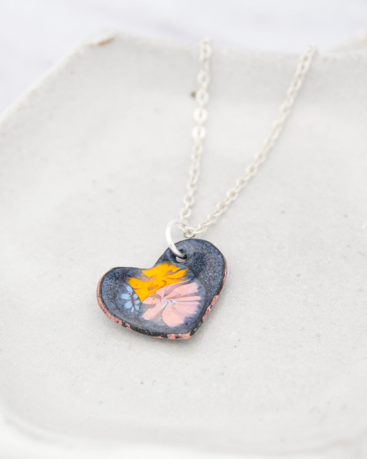 A heart-shaped pendant with a colorful floral design is displayed on a white surface.