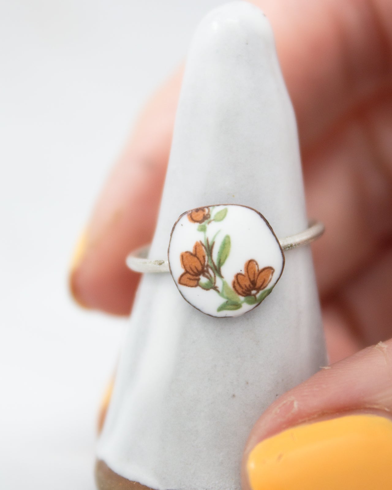 A hand is holding a white ring with a floral design on it.