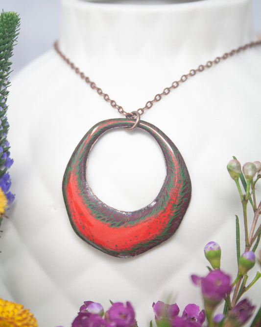 A necklace with a large, colorful pendant is displayed against a white background, surrounded by flowers.