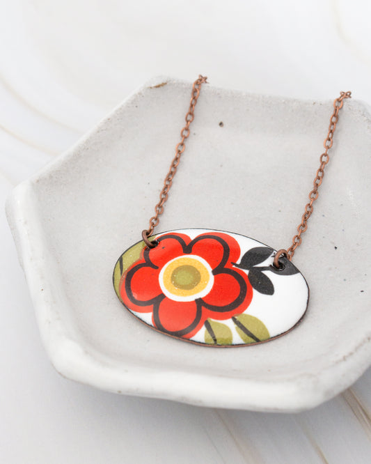 A necklace with a pendant featuring a red flower design is displayed on a white plate.