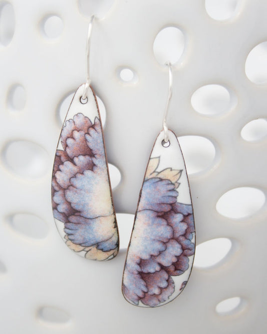 A pair of earrings with a floral design on the pendants, hanging against a white background with a perforated pattern.