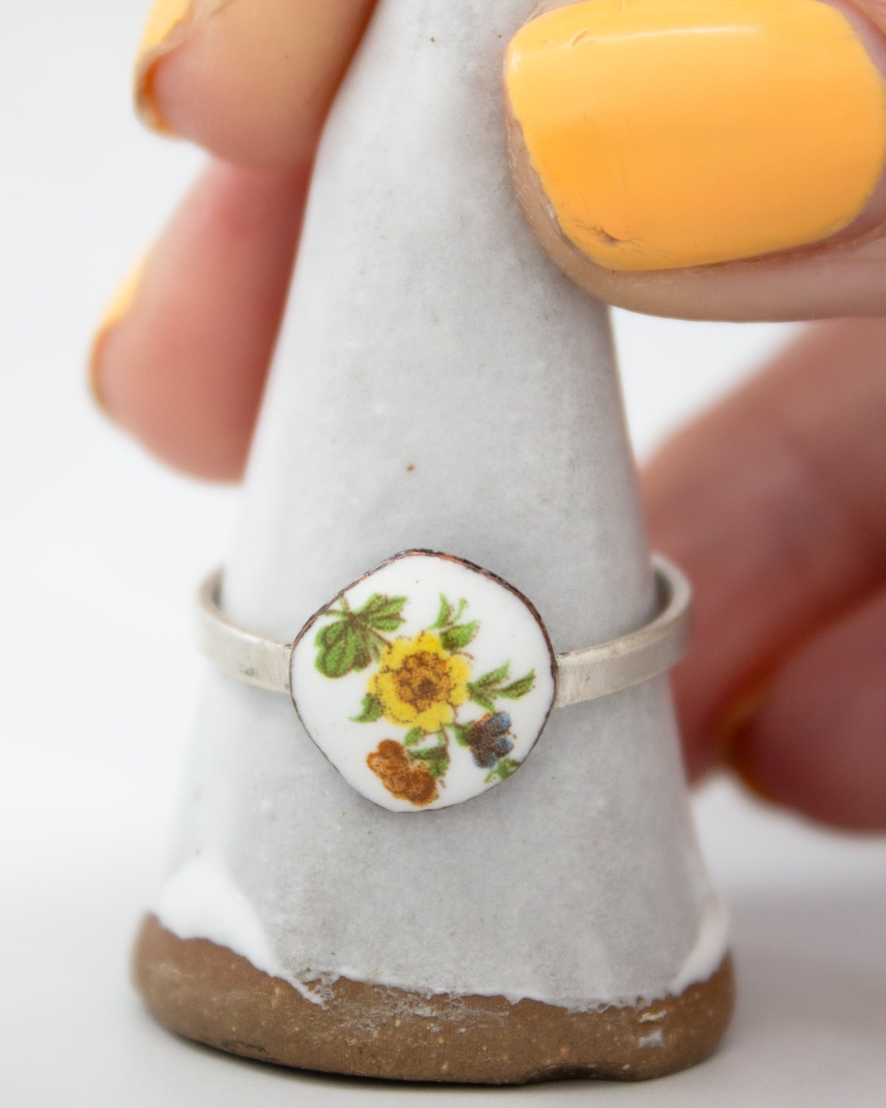 A hand is holding a white ceramic ring with a floral design on it, which is placed on a white stand.