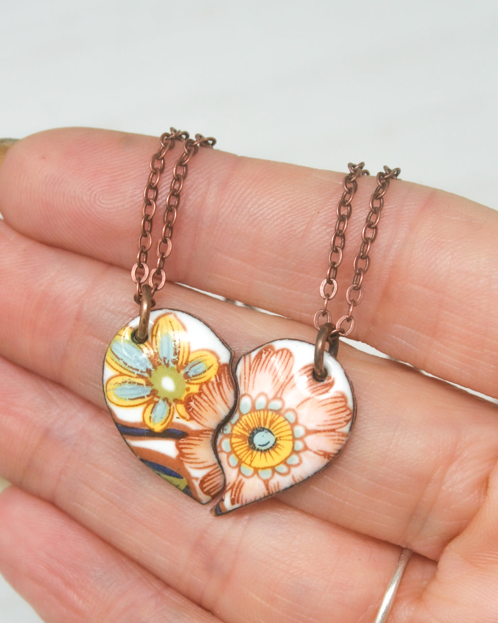 a hand holding a heart shaped pendant with flowers on it