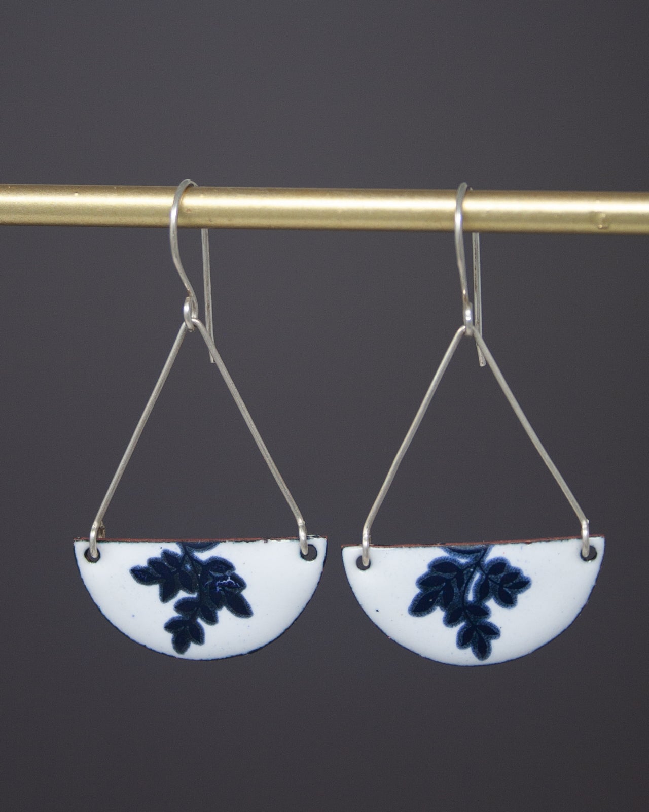 A pair of earrings with white and blue floral designs hanging from a gold-colored metal hook.