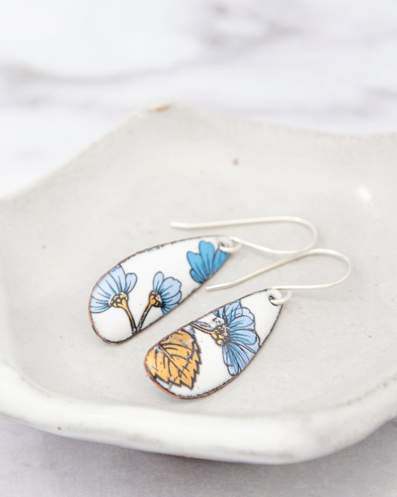 A pair of earrings with blue and yellow floral designs on a white plate.