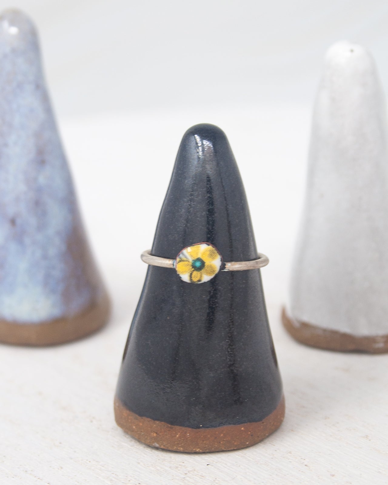 A black ceramic ring stand with a yellow flower design on it, placed between two white ceramic stands.