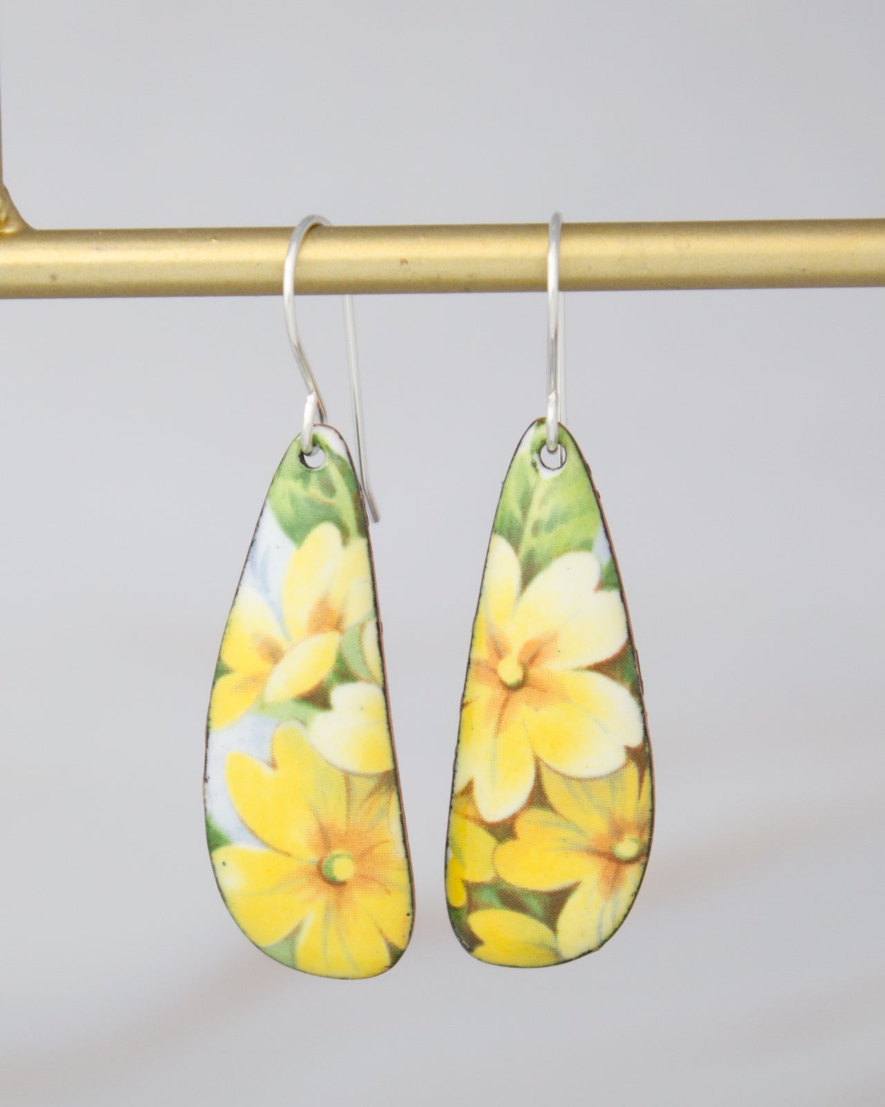 A pair of earrings with yellow flower designs hanging from a gold-colored metal hook.