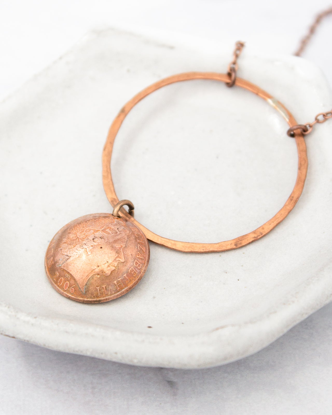 A necklace with a pendant featuring a coin design, resting on a white surface.