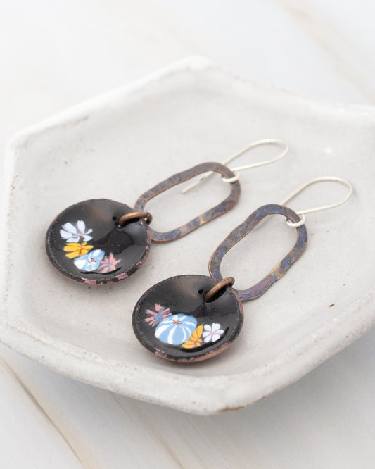 A pair of black earrings with colorful floral designs on them, displayed on a white plate.