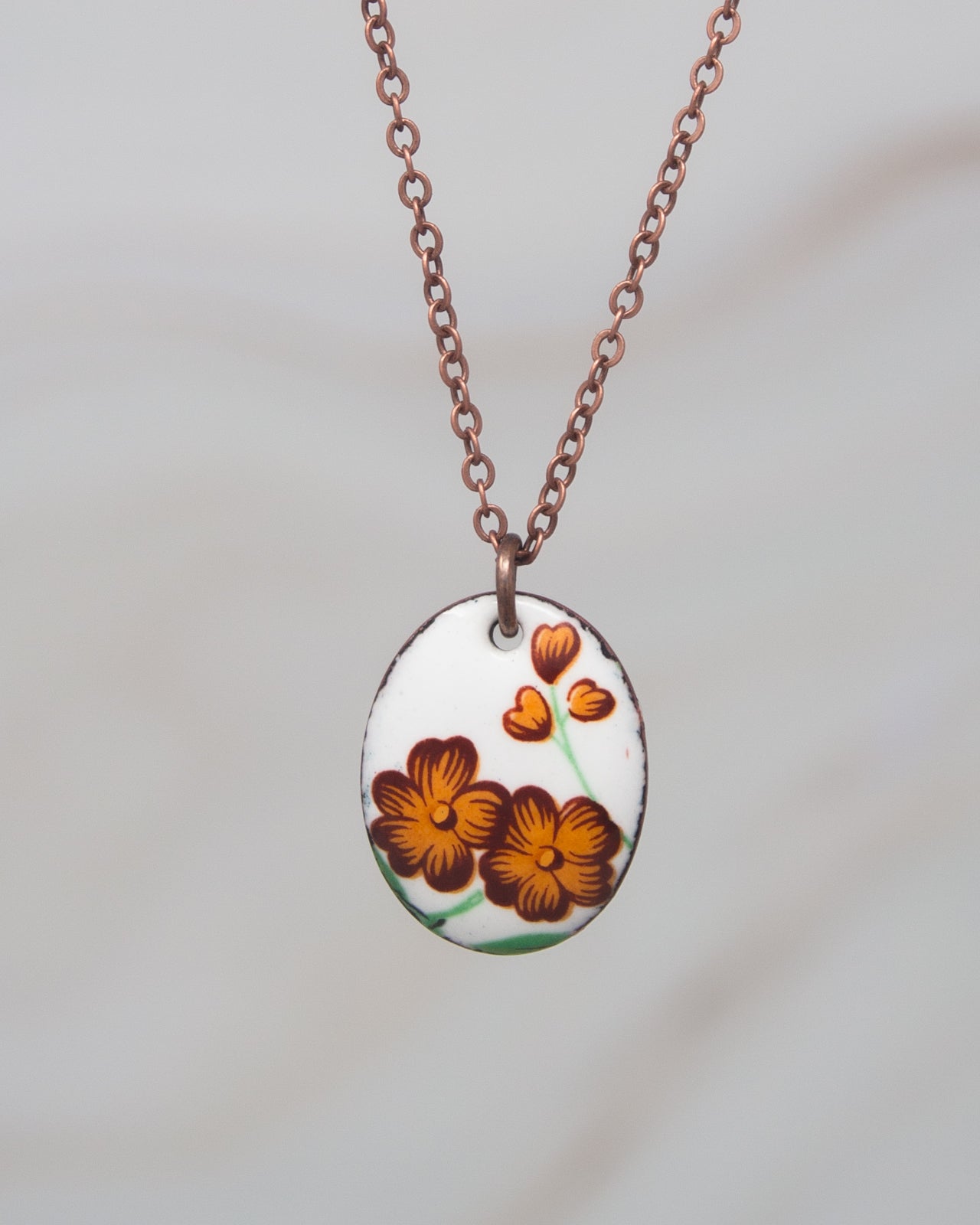 A necklace with a pendant featuring a floral design in shades of orange and brown.